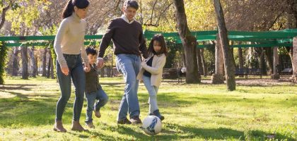 A family plays soccer together in a sunny park, enjoying quality time outdoors.